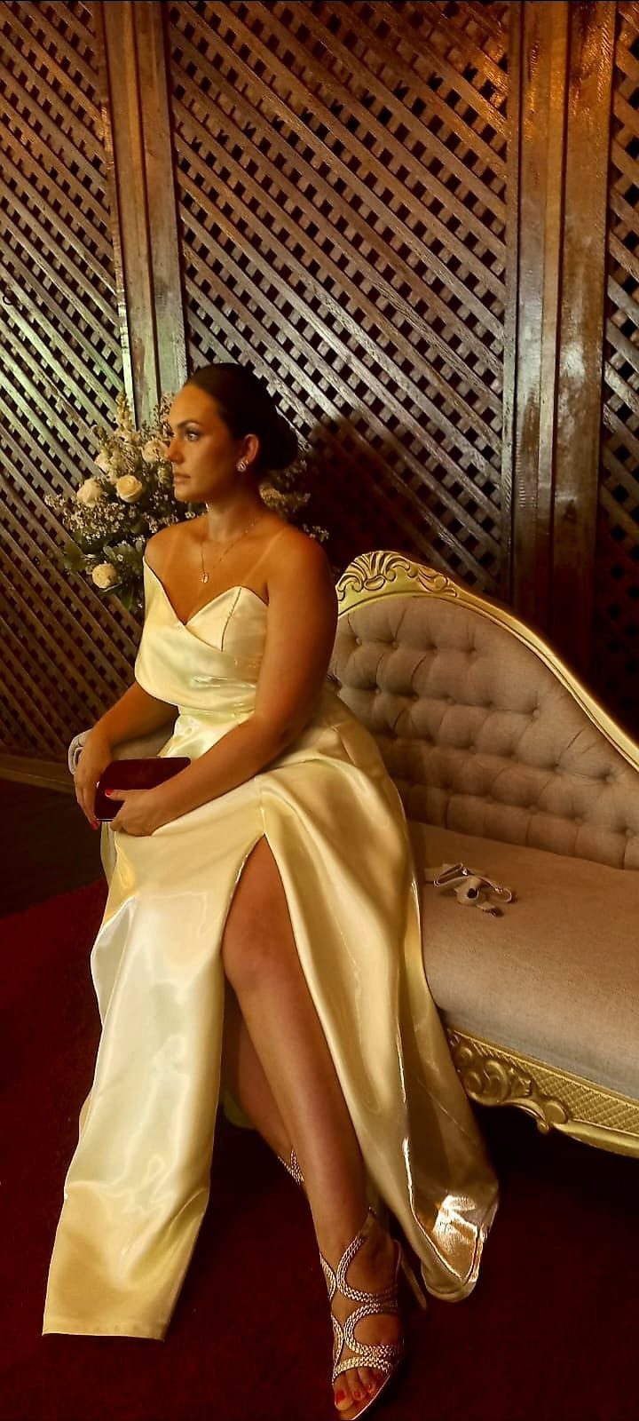 Mulher de vestido de cetim champanhe com fenda, sentada em um divã