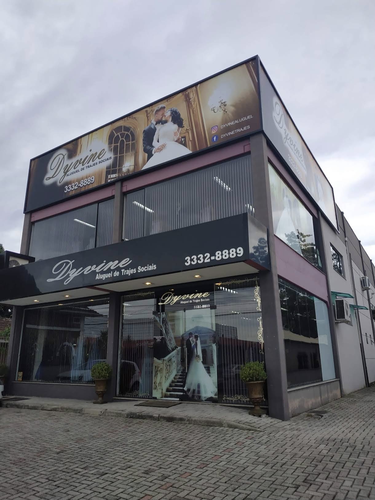 Fachada da loja Dyvine Aluguel de Trajes Sociais na Rua Dr. Nereu Ramos, em Gaspar, com outdoor de noivos e o telefone 3332-8889