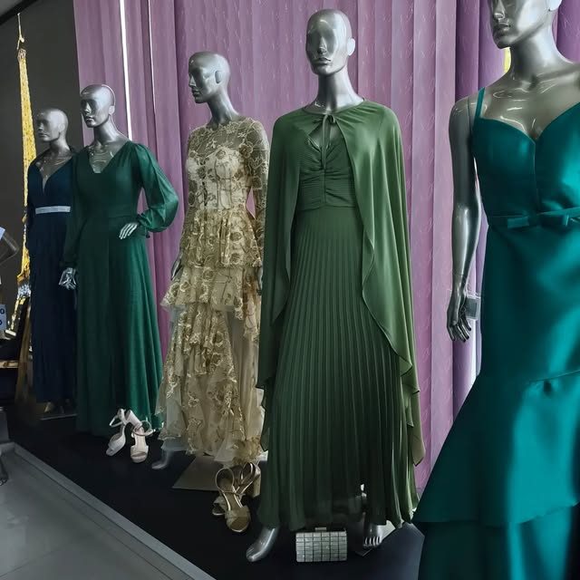 Vitrine com vestidos de festa verdes e dourados em manequins